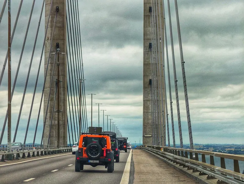 Jeeps fahren in Kolonne über eine große Schrägseilbrücke