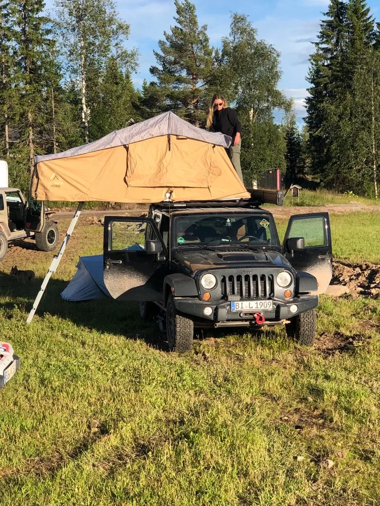 Jeep Wrangler mit Dachzelt auf einem Stellplatz zwischen Nadelbäumen