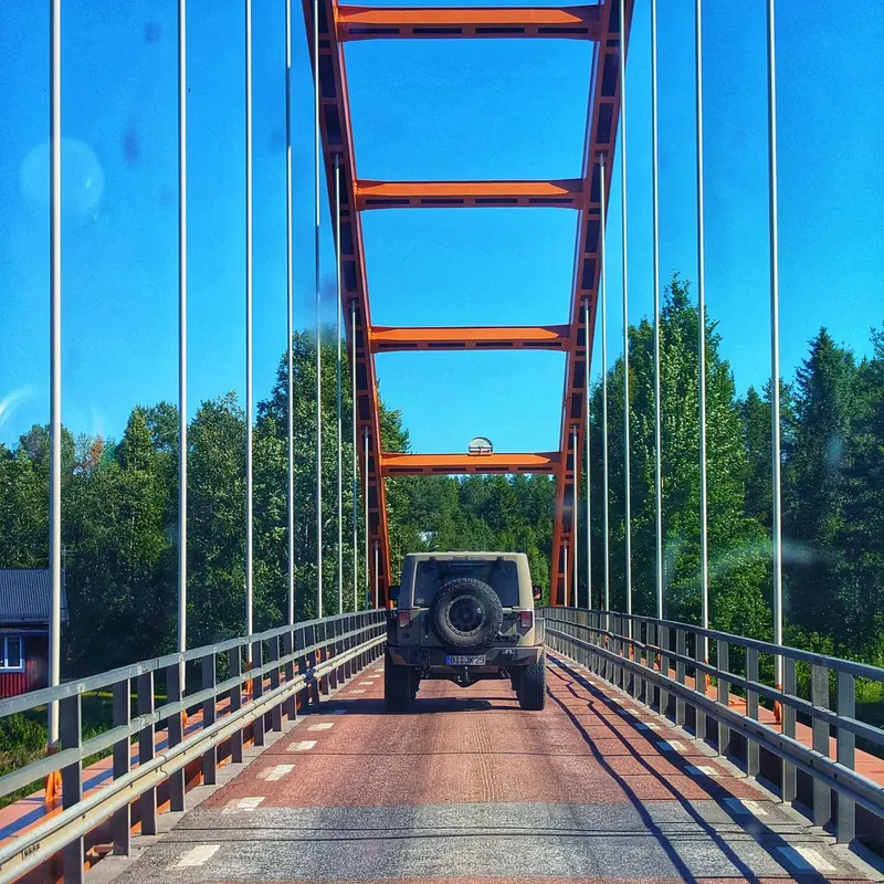 Jeep fährt über eine Brücke mit orangem Stahlbogen
