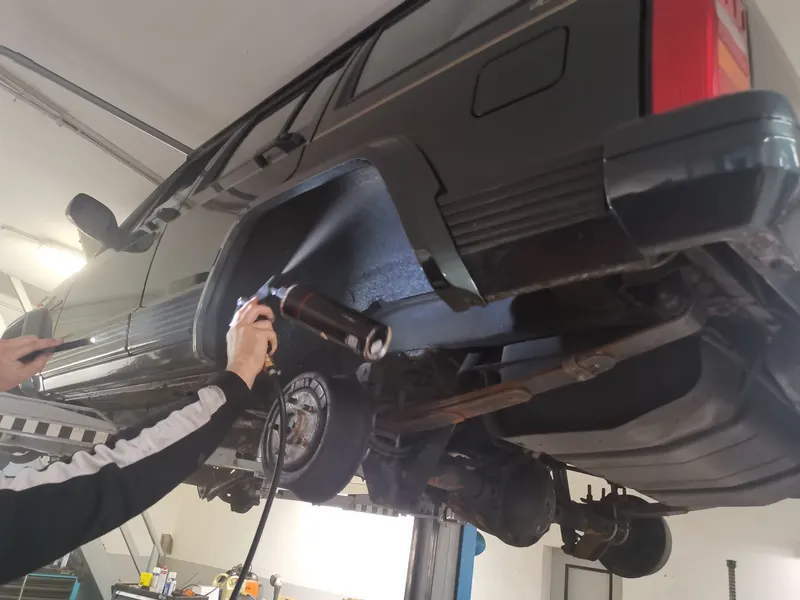 Der Radlauf eines Jeep Cherokee auf der Hebebühne wird mit einer Sprühpistole behandelt