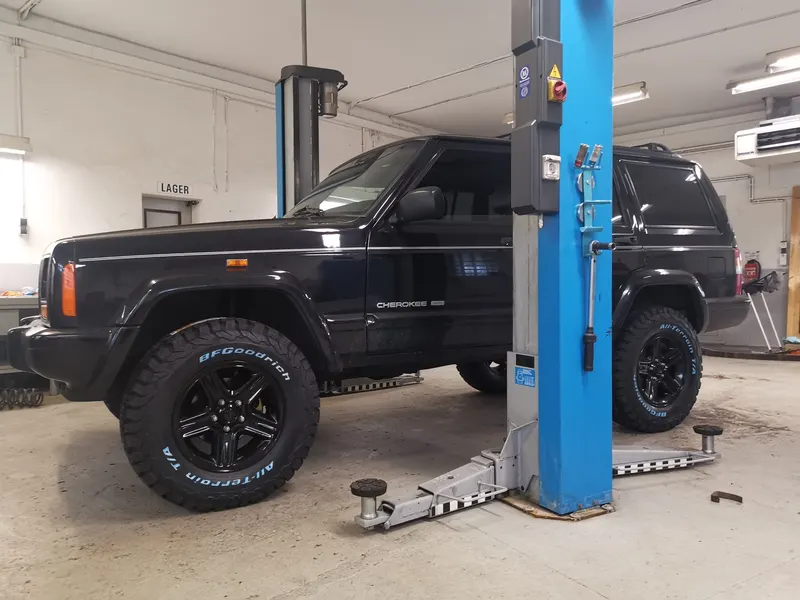 Schwarzer Jeep Cherokee mit Offroad-Reifen auf der Hebebühne in der Werkstatt