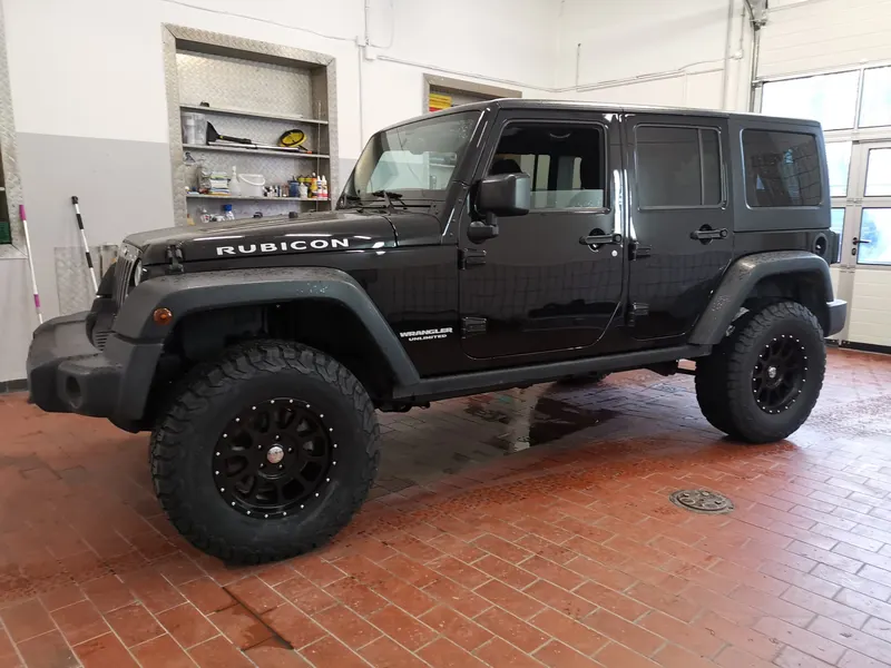 Schwarzer Jeep Wrangler Rubicon mit höhergelegtem Fahrwerk und schwarzen Felgen in der Werkstatt