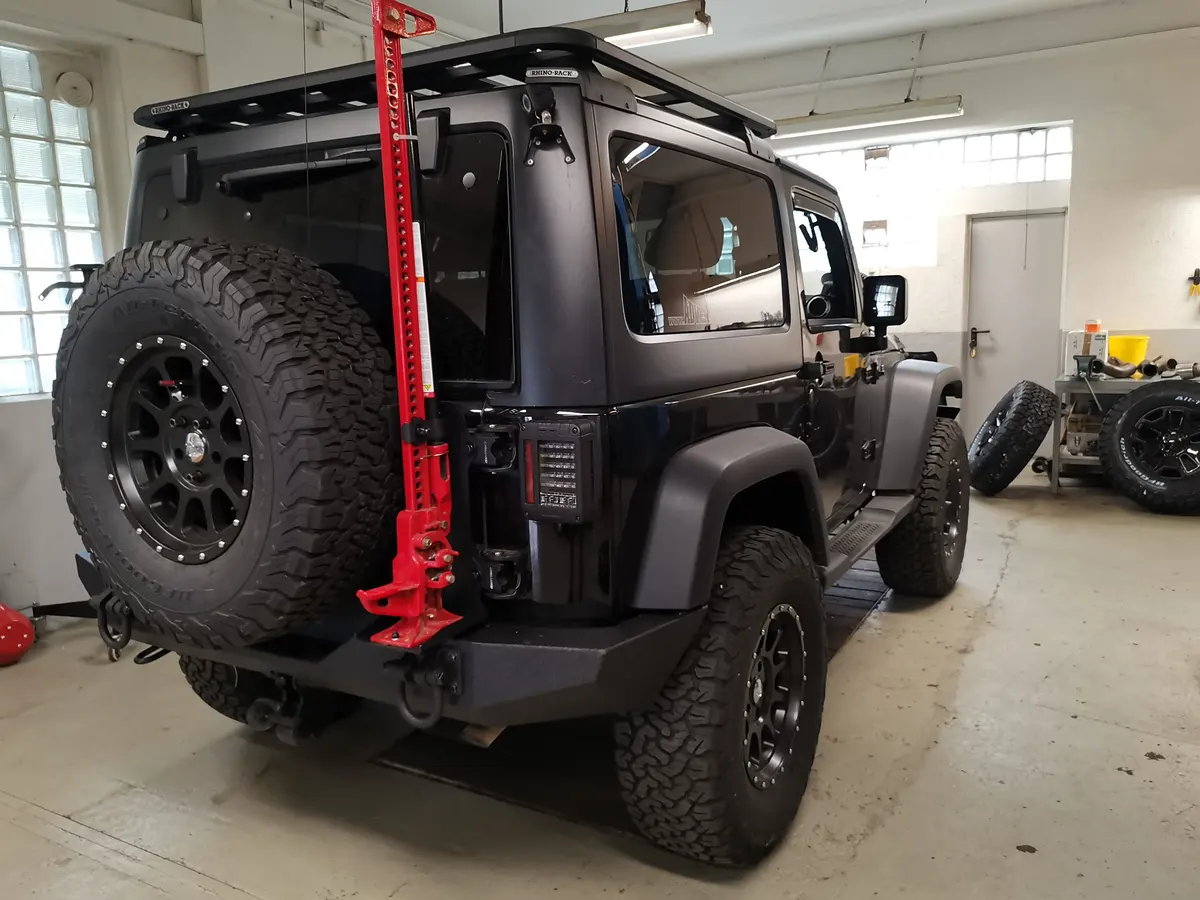 Heck eines schwarzen Jeep Wrangler mit Dachträger, Reserverad und rotem Wagenheber