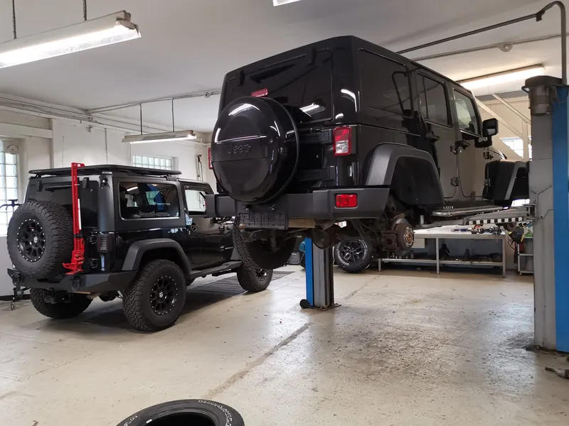 Zwei schwarze Jeep Wrangler in der Werkstatt, einer auf der Hebebühne