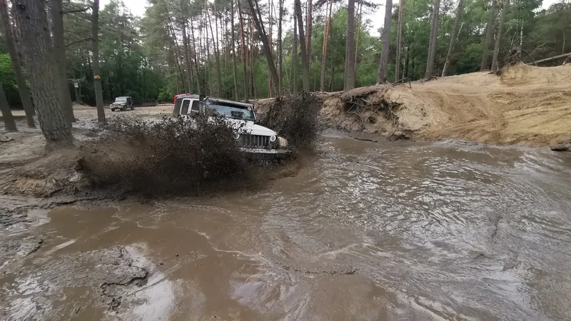 Jeep pflügt mit viel Spritzwasser durch ein Schlammloch