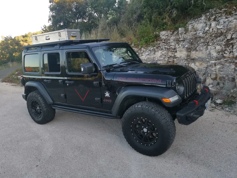 Schwarzer Jeep Wrangler mit Dachbox an einer Felswand