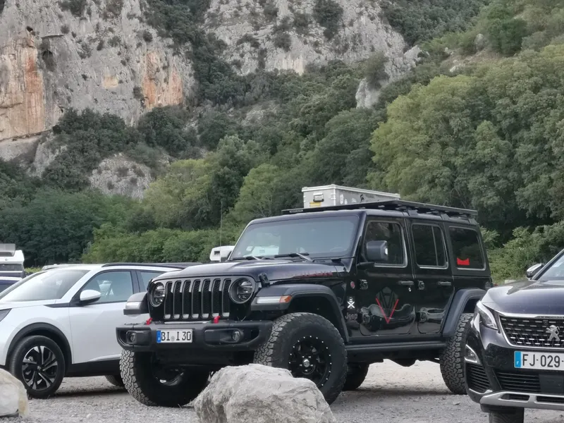 Schwarzer Jeep Wrangler mit Dachbox auf einem Parkplatz vor Kalkfelsen