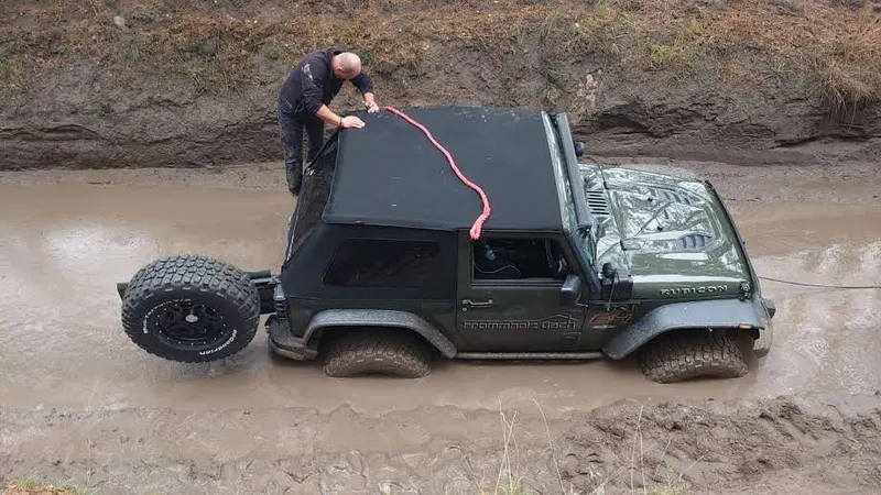 Teilnehmer befestigt ein Bergeseil an einem Jeep im Schlammloch