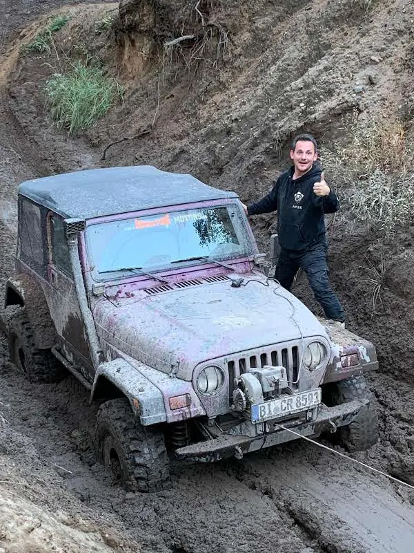 Teilnehmer neben einem schlammverschmierten Jeep am Hang