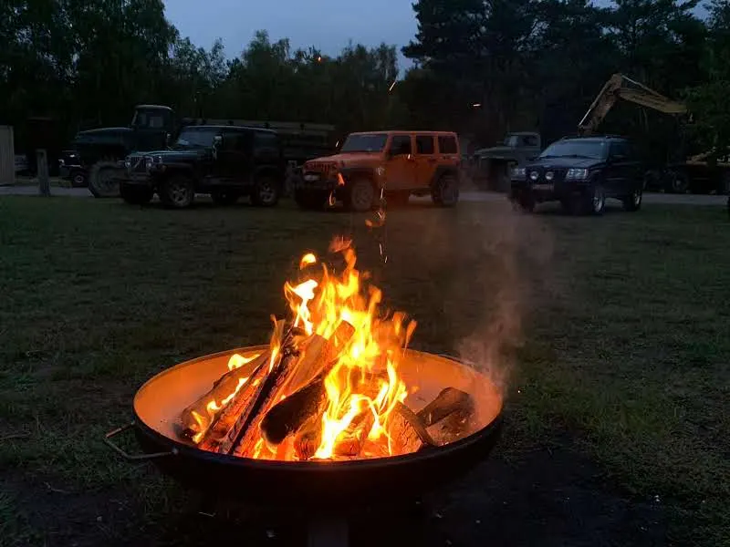 Feuerschale mit Lagerfeuer in der Dämmerung, dahinter geparkte Jeeps