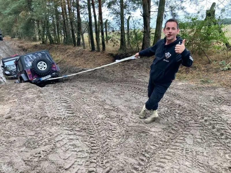 Teilnehmer zieht lachend an einem Bergeseil, das an einem festgefahrenen Jeep hängt