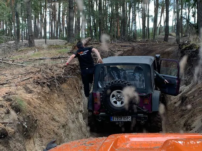 Jeep fährt durch einen engen Graben, ein Teilnehmer klettert daneben