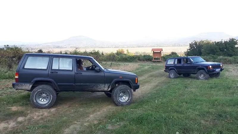 Zwei Jeep Cherokee auf einer Wiese mit Bergen im Hintergrund