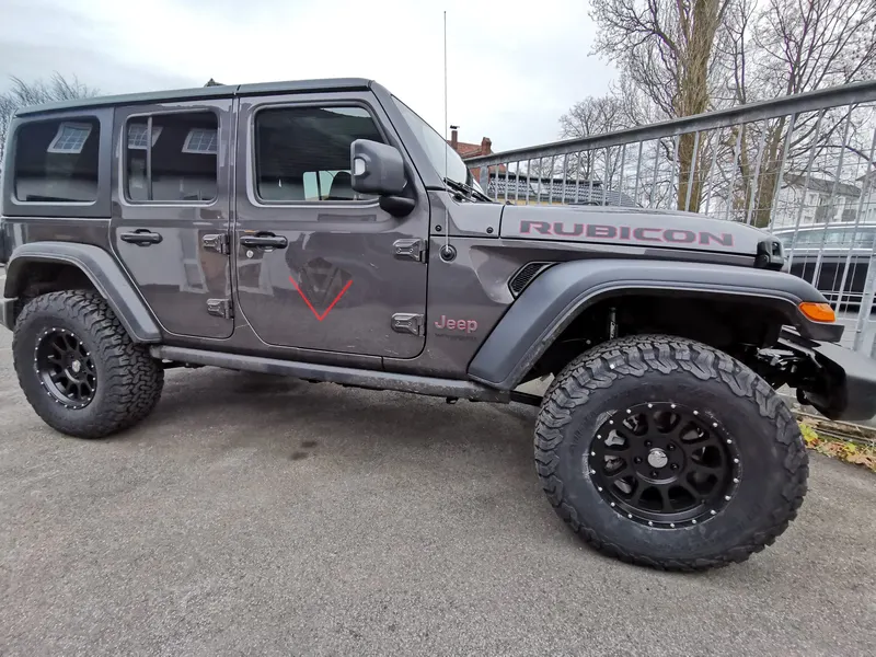 Grauer Jeep Wrangler Rubicon mit Höherlegung und Offroad-Reifen auf dem Hof