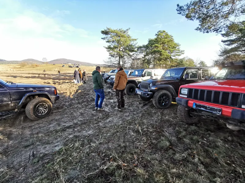Jeeps und Teilnehmer auf schlammigem Gelände unter blauem Himmel