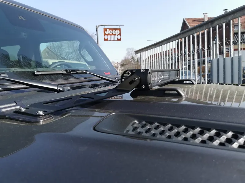 Jeep-Motorhaube mit Lichtleisten-Halterung am Scharnier, im Hintergrund das Jeep-Schild