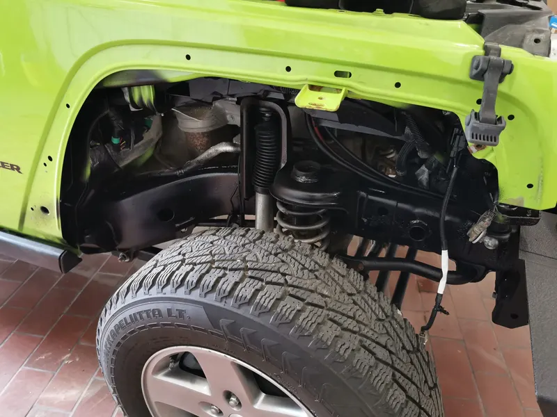 Radlauf eines limettengrün lackierten Jeep Wrangler in der Werkstatt: Kotflügel, Vorderachse mit Feder und Reifen ohne Verkleidung