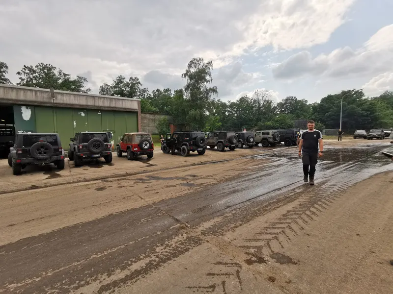Reihe von Jeeps auf einer nassen Sandfläche vor einer Halle