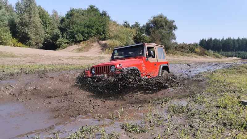 Roter Jeep Wrangler fährt durch eine Schlammpfütze
