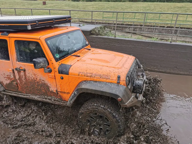 Oranger Jeep Wrangler mit Dachzelt im Schlamm