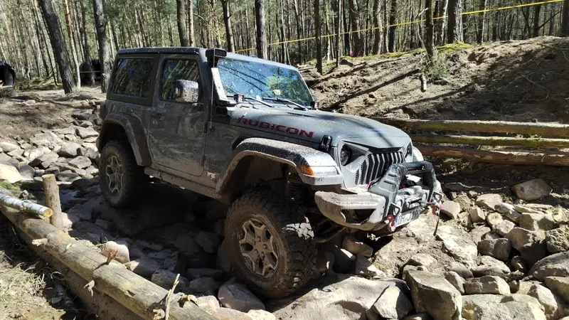 Grauer Jeep Wrangler klettert über Felsbrocken und Baumstämme