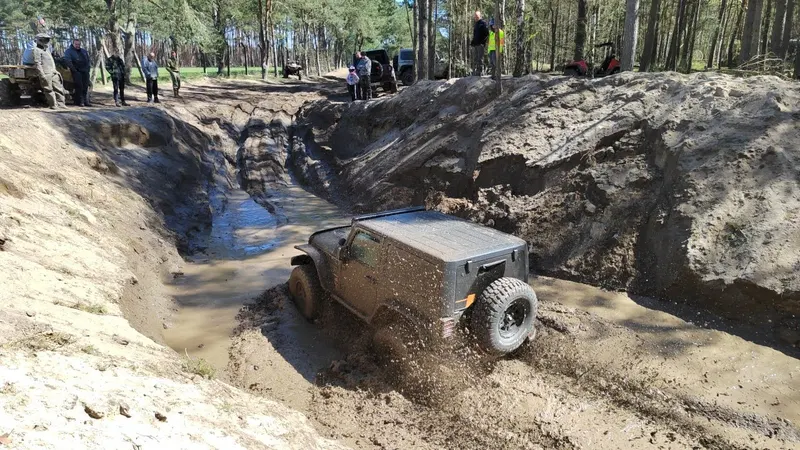 Jeep kämpft sich durch eine schlammige Rinne, Zuschauer am Rand
