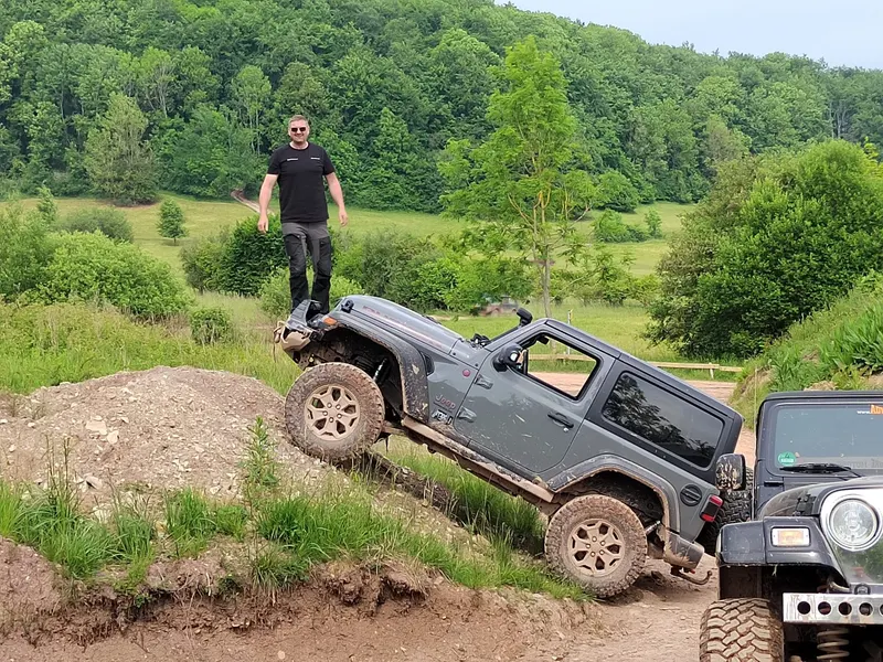 Jeep Wrangler fährt eine Böschung hinauf, oben steht ein Mann