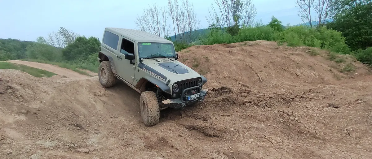 Grüner Jeep Wrangler fährt über einen Erdhügel