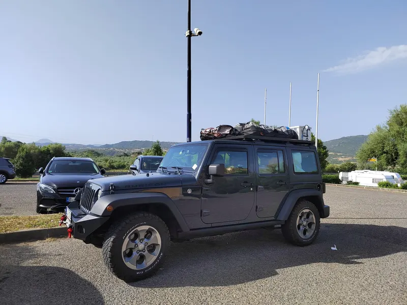 Grauer Jeep Wrangler mit Dachträger auf einem Parkplatz am Meer