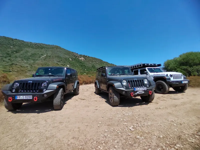 Drei Jeeps auf einer Sandpiste vor grünen Hügeln