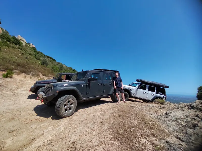 Jeeps auf einer Anhöhe über dem Meer, daneben ein Teilnehmer