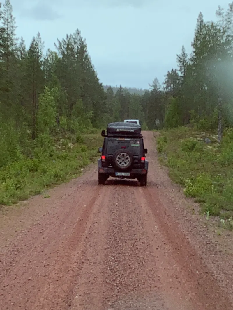 Roter Jeep auf einer langen Schotterpiste durch den Wald
