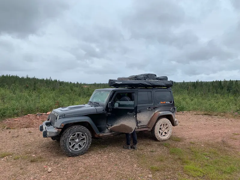 Grauer Jeep Wrangler mit Dachzelt auf einer Lichtung